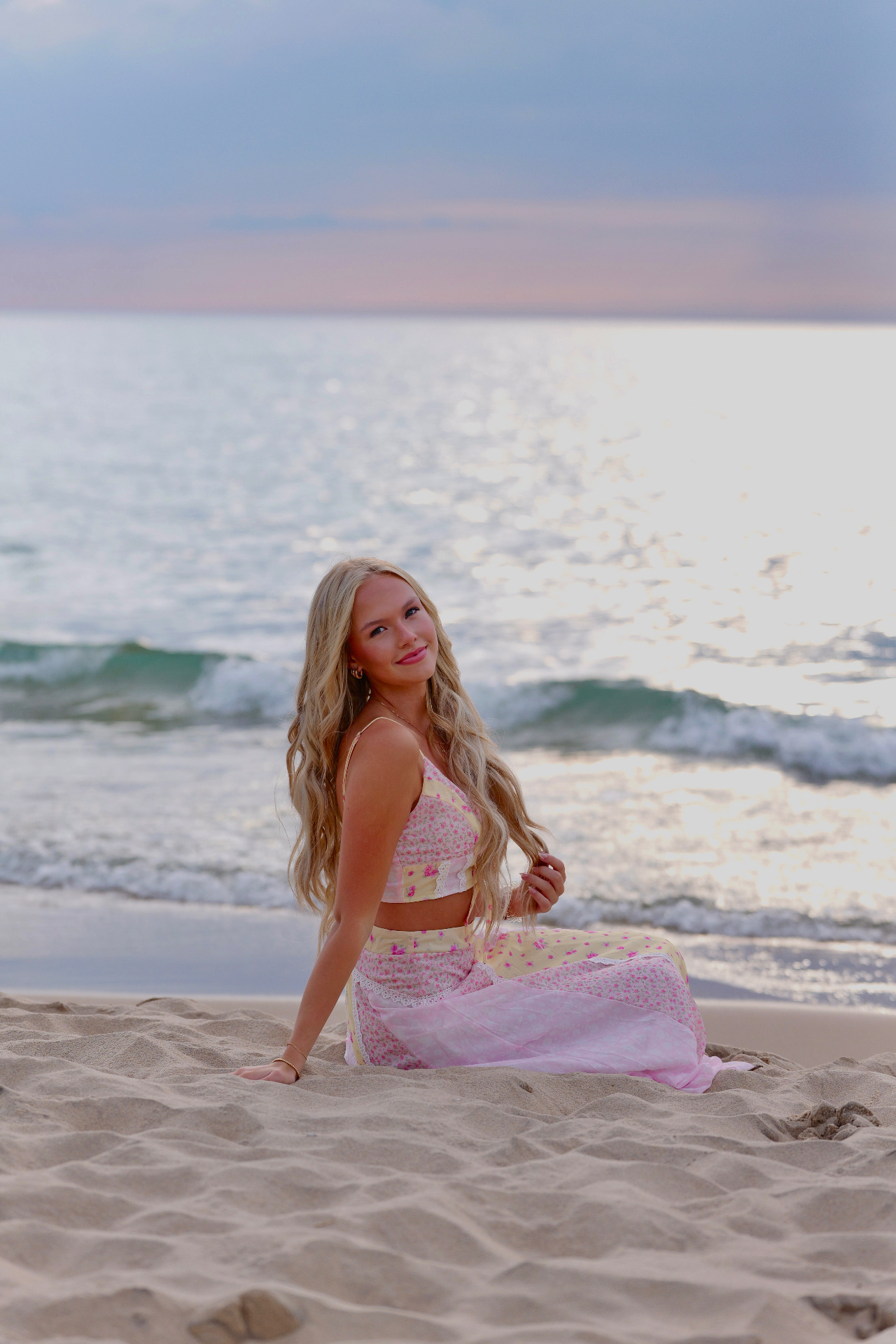 Ellis Jayne sitting on the shoreline at sunset in a pink and yellow floral set
