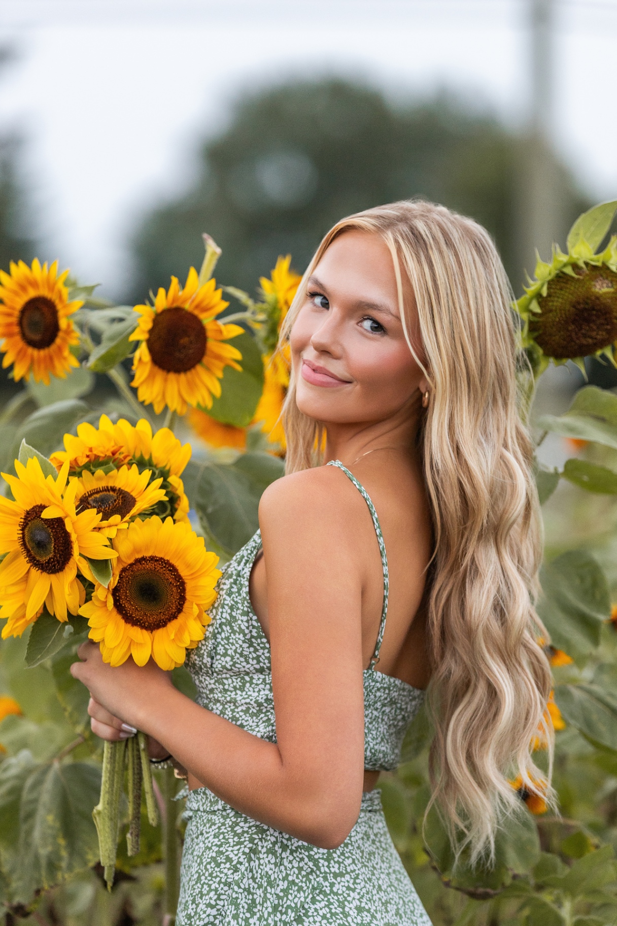 Ellis Jayne looking over her shoulder in a green floral dress holding sunflowers