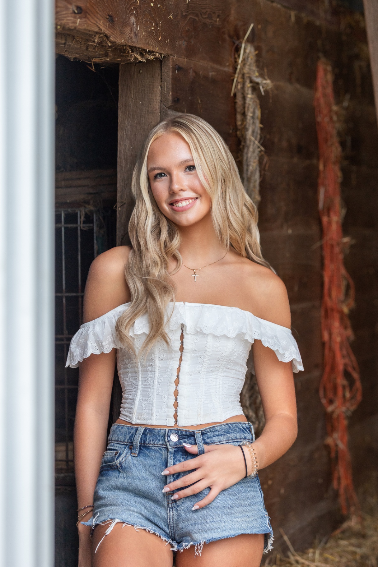 Ellis Jayne standing in a barn doorway in a white eyelet top and denim shorts